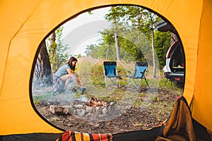 view from camping tent woman cooking on burner near bonfire