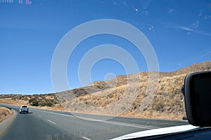 View from a car on an asphalt road in the desert in perspective with a car driving ahead