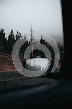 View from a car of fog on a road under pikes peak mountains trees in Colorado, vertical shot