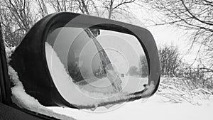 View from the car in the rearview mirror while driving on a snowy winter road. Extreme road conditions