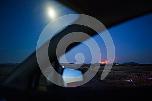 View from Car towards Volcanic Eruption at Grindavik in Iceland with Full Moon at Night