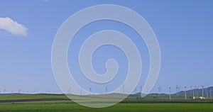 View from car of wind turbine farm spinning in green summer field on a sunny day