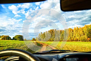 View from car window on beautiful landscape with field and road. Autumn nature with sky full of white clouds. Travel concept