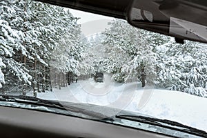 View from car window on off-road vehicle driving on winter forest road, snow covered trees. Extreme winter sport, travel