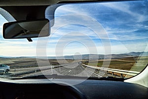 View from car window on the road and strange landscape with a valley, mountains and blue sky with clouds. Landscape through