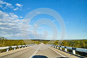 View from car windscreen with stripe relief to highway, tundra and blue sky in norht region at a sunny day