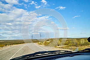 View from car windscreen with stripe relief to highway, tundra and blue sky in norht region at a sunny day