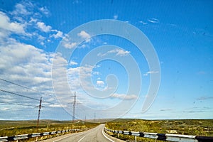 View from car windscreen with stripe relief to highway, tundra and blue sky in norht region at a sunny day