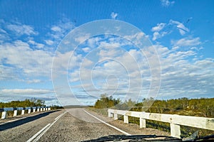 View from car windscreen with stripe relief to highway, tundra and blue sky in norht region at a sunny day