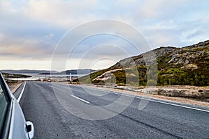 View from car windscreen to highway, tundra and hills in evening time. Polar day in Norway