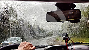 View from the car windshield from the driver's seat and hand on the steering wheel of woman on during rain, drops on
