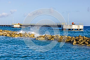 View of the Caribbean Sea with a pier and an artificial breakwater where waves crash against the rocks.