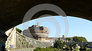 View of Castel Sant`Angelo from a bank of the Tiber river, framed by the shadow of a bridge