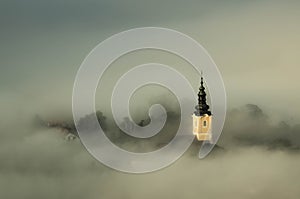 View of a castle with a black roof covered in fog with a forest on the background during a storm