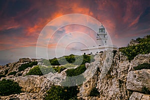 View of Cavalleria lighthouse with rocky cliff during a summer day with dramatic cloudy sunset in the balearic island of Menorca