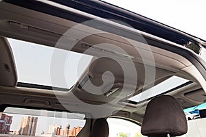 View of the ceiling of the car with a transparent double glass hatch for airing, opening so that you can see the sky and clouds in