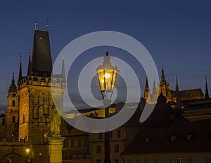 View from Charles Bridge on Mala Strana bridge tower with glowing street lamp nad Prague Castle at night, dark blue sky