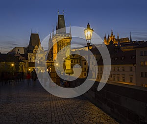 View from Charles Bridge on Mala Strana bridge tower with glowing street lamp nad Prague Castle at night, dark blue sky