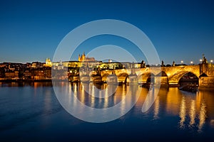 View on Charles Bridge and Prague Castle over Vltava River during early night with wonderful blue sky and yellow city