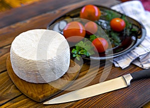 View of cheese head on wooden board served with tomatoes and fresh greens. Serving French homemade cheese. Food concept