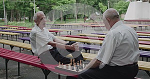 View of chess game between elder, thoughtful men having relax on outdoors bench