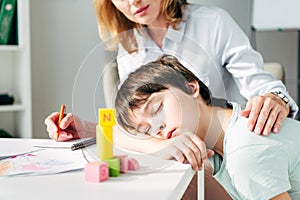 View of child psychologist hugging kid with dyslexia sleeping on table
