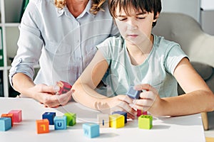 View of child psychologist and kid with dyslexia playing with building blocks