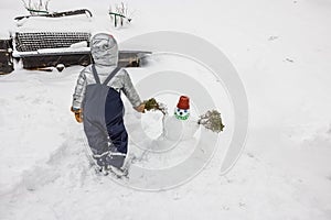 View of a child by a self-made cute snowman in a snowy garden.