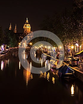 View of a church and a canal in Amsterdam, Netherlands at night. The Basilica of Saint Nicholas Sint-Nicolaasbasiliek with the r