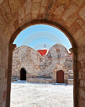 View of the church courtyard and the old church building through the arch of the bell tower in the Greek village of Asklipio in Rh