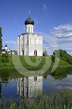 View of the church of Pokrova-na-Nerli and its reflection in the river among trees and meadows in Bogolyubovo, Russia