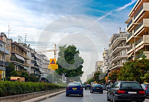 View of the city. Cars moving down the street. On the sides of street are high-rise buildings. Big crane on the horizon