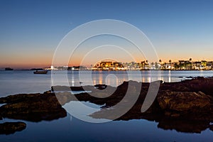 View of city lights and the sea in the foreground in the evening in  Porto Cesareo, Italy