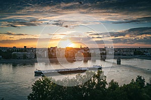 View of the city of Novi Sad and Danube river Strand bridge at sunset from the Petrovaradin fortress. A barge floats on the river