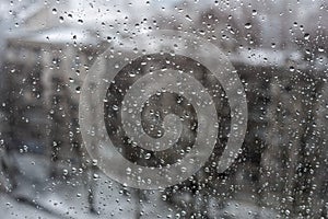 View of the city in a snowfall through a window covered with water drops.