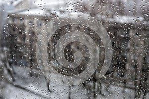 View of the city in a snowfall through a window covered with water drops