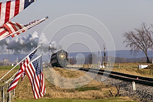 View of a Classic Steam Passenger Train Approaching, With American Flags Attached to a Fence
