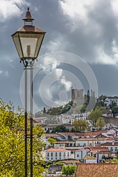 View of a classic traditional lamppost, public electric light and castle and fortress of Obidos, as background