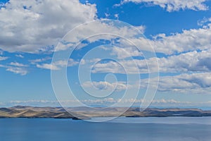 View of clear calm undulating blue water of Lake Baikal, mountains on the horizon, blue cky, white clouds