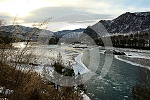 A view of a clearing on a river flowing through a snow-covered valley in the mountains in early winter