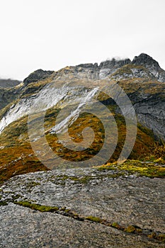 View from a cliff edge in the mountains of Lofoten Islands in Norway into a valley with a waterfall and lake