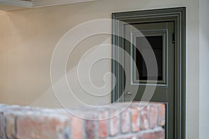 View of a closed door inside an office or cafe. Beige tiles on the floor and granite baseboards along the wall. Evacuation exit