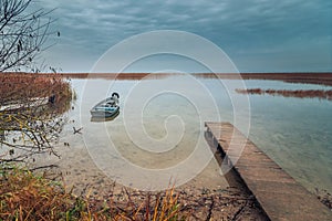 view from the coast of the lake to a beautiful water landscape with a boat, wooden pier and coastal reeds in the light of autumnal