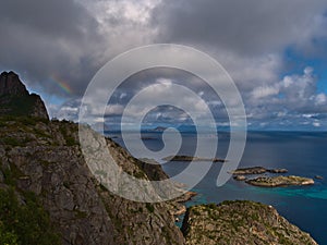 View of coast of Norwegian Sea on AustvÃ¥gÃ¸ya island near HenningsvÃ¦r, Lofoten, Norway with rugged mountains and rainbow.