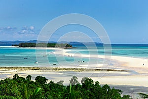 View of coastline of Iranja Island, Nosy Iranja lined with palm trees and boats floating in the sea, Madagascar