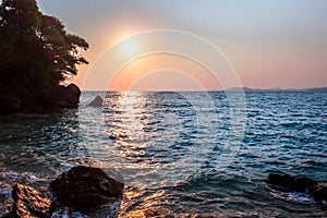 View of coastline on Nosy Komba Island lined with palm trees and boats floating in the sea at sunset, Nosy Komba