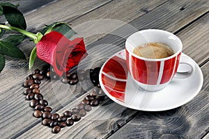 View of a coffee cup on a wooden table old adorned with a red rose and coffee beans.