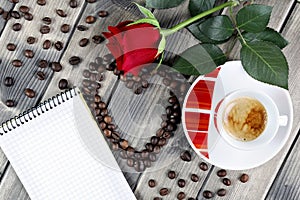 View of a coffee cup on a wooden table old adorned with a red rose and coffee beans.
