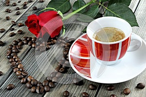 View of a coffee cup on a wooden table old adorned with a red rose and coffee beans.