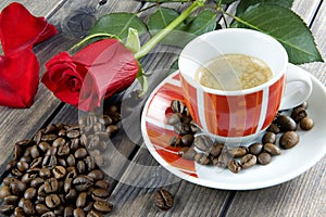 View of a coffee cup on a wooden table old adorned with a red rose and coffee beans.